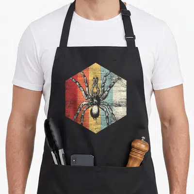 Tarantula halloween apron - Grey spider illustration on hexagon with red orange yellow blue white distressed stripes — shown on a black cotton canvas apron against a white background