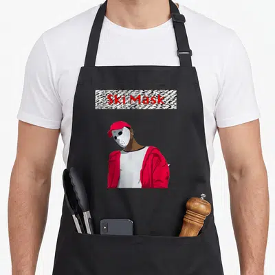 Ski slump apron - Cartoon person in white mask and red jacket below zebra print rectangle with red text — shown on a black cotton canvas apron against a white background