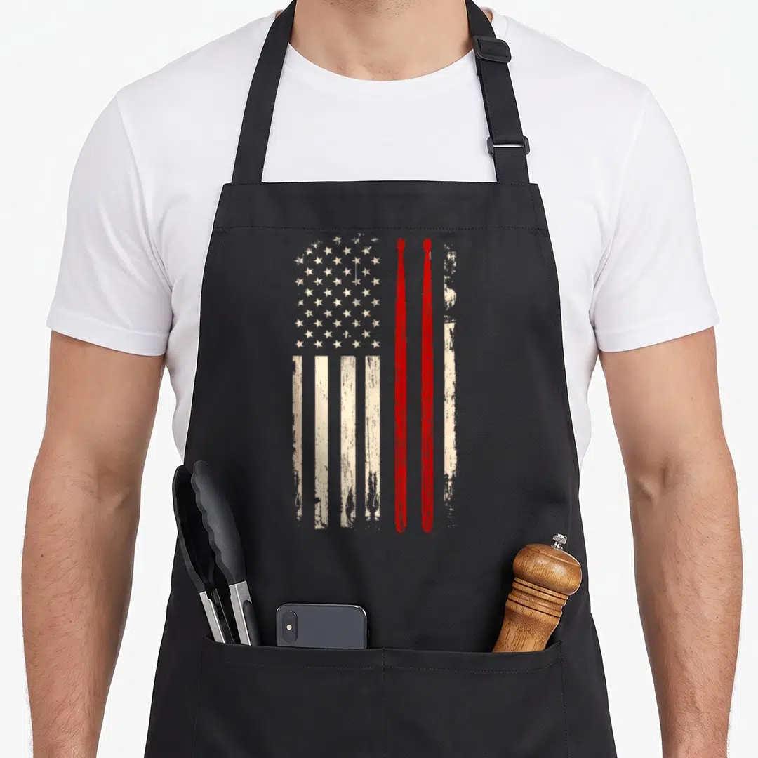 Stick american flag apron - Distressed USA flag with two vertical red drumsticks overlapping the right side — shown on a black cotton canvas apron against a white background