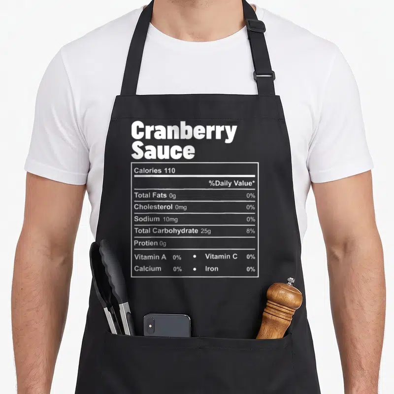 Food cranberry thanksgiving apron - White nutrition label text showing 110 calories and 0g fat for cranberry sauce — shown on a black cotton canvas apron against a white background