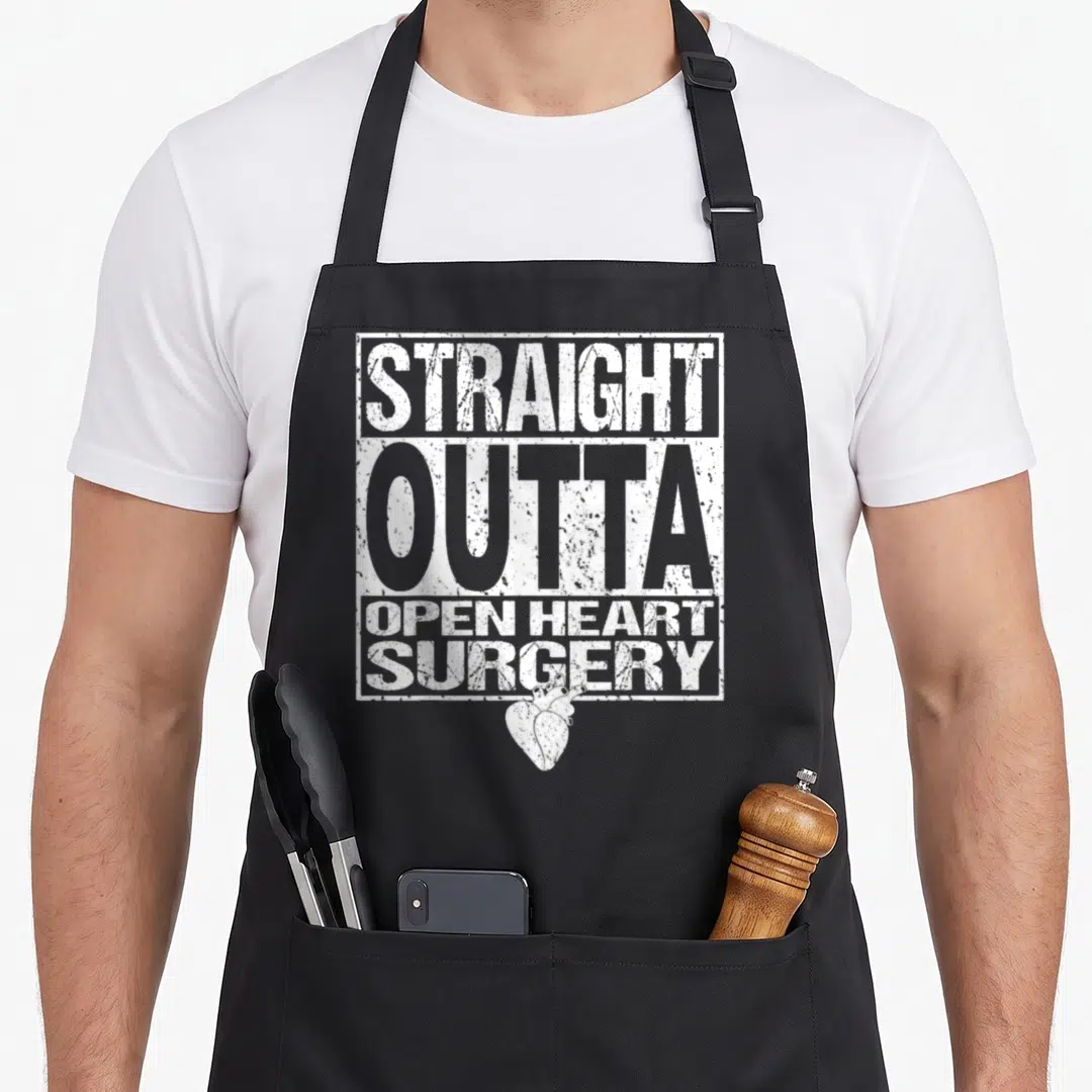 Attack open apron - Distressed white text reading STRAIGHT OUTTA OPEN HEART SURGERY above anatomical heart — shown on a black cotton canvas apron against a white background