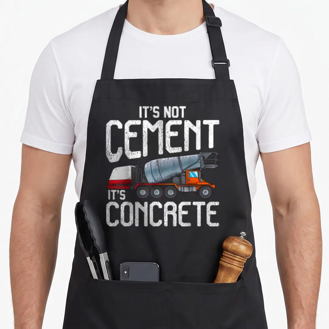 Cement truck apron - Distressed concrete mixer truck with IT'S NOT CEMENT IT'S CONCRETE text in white grey orange — shown on a black cotton canvas apron against a white background