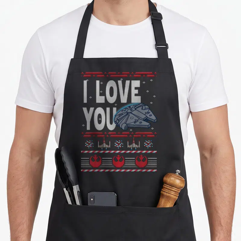 Ugly falcon apron - Knit-style I LOVE YOU text with Millennium Falcon and X-wing borders in white, red, and blue — shown on a black cotton canvas apron against a white background