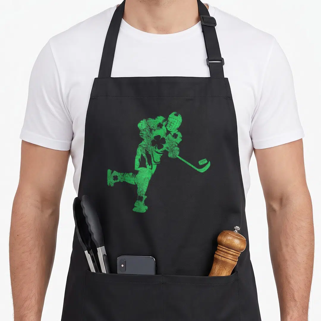 Hockey st patrick day aprons - Green distressed silhouette of a hockey player swinging a stick on a black background — shown on a black cotton canvas apron against a white background