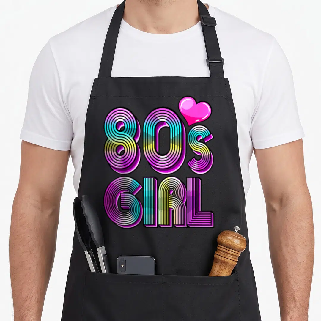 80s birthday apron - Retro 80S GIRL text in purple blue yellow pink with pink heart graphic — shown on a black cotton canvas apron against a white background