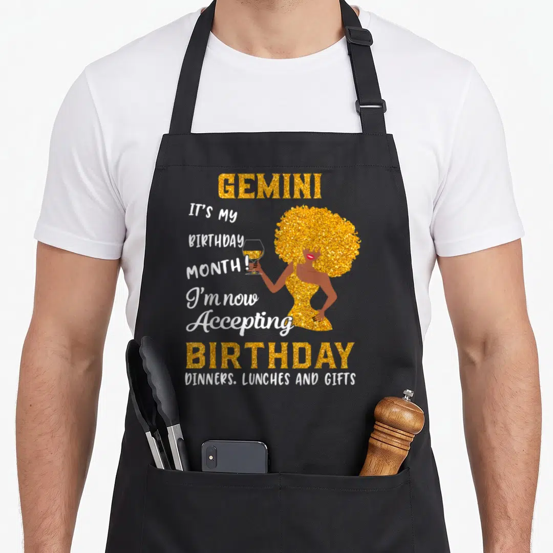 May june birthday apron - Gold glitter cartoon woman holding wine glass with Gemini birthday acceptance text — shown on a black cotton canvas apron against a white background