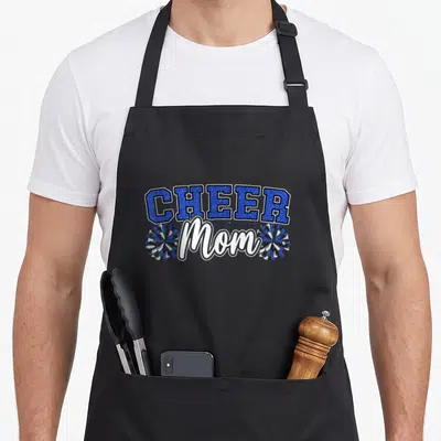 Cheer mama apron - Blue arched CHEER text above white Mom script flanked by two cartoon pom-poms in blue white and black — shown on a black cotton canvas apron against a white background