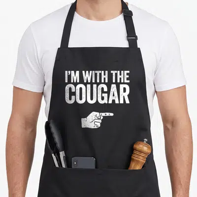 Costume cougar apron - White distressed text I'M WITH THE COUGAR above pointing hand on black apron — shown on a black cotton canvas apron against a white background