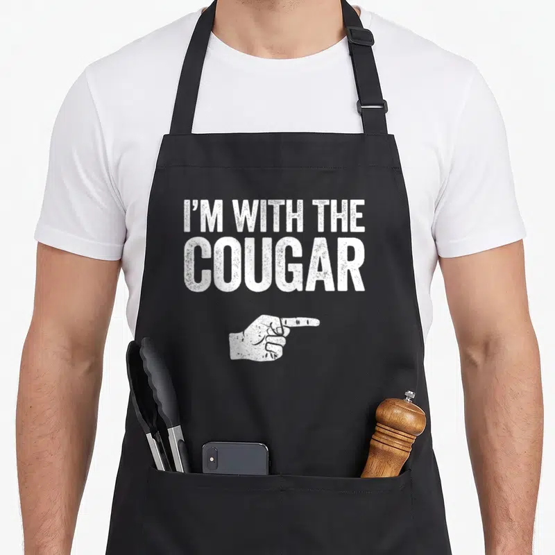 Costume cougar apron - White distressed text I'M WITH THE COUGAR above pointing hand on black apron — shown on a black cotton canvas apron against a white background