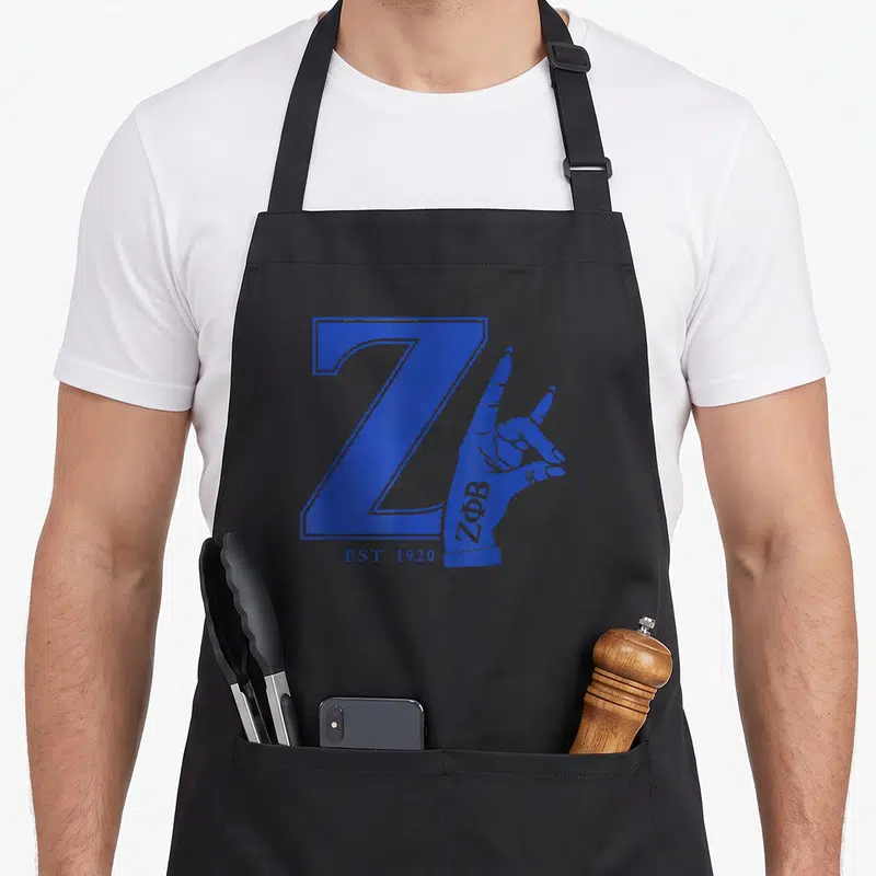 Est 1920s apron - Blue letter Z with hand making gesture and Greek letters ZΦΒ on wrist below EST 1920 — shown on a black cotton canvas apron against a white background