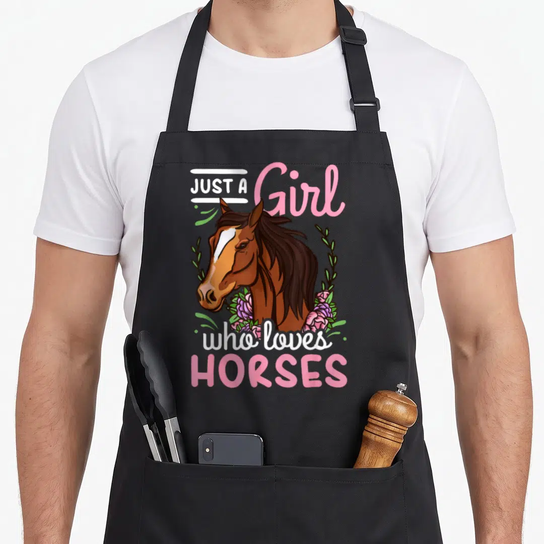 Jumping horse apron - Cartoon brown horse head with pink flowers and text Just a Girl who loves Horses — shown on a black cotton canvas apron against a white background