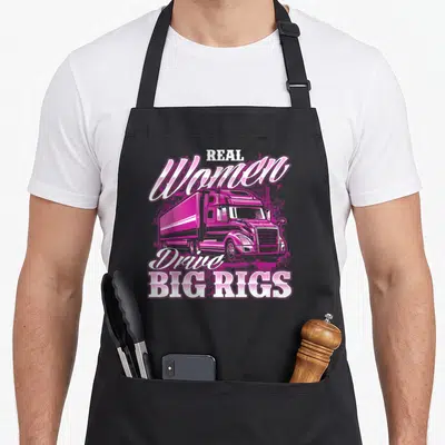 Drive semi truck apron - Pink cartoon semi-truck with Real Women Drive Big Rigs text — shown on a black cotton canvas apron against a white background