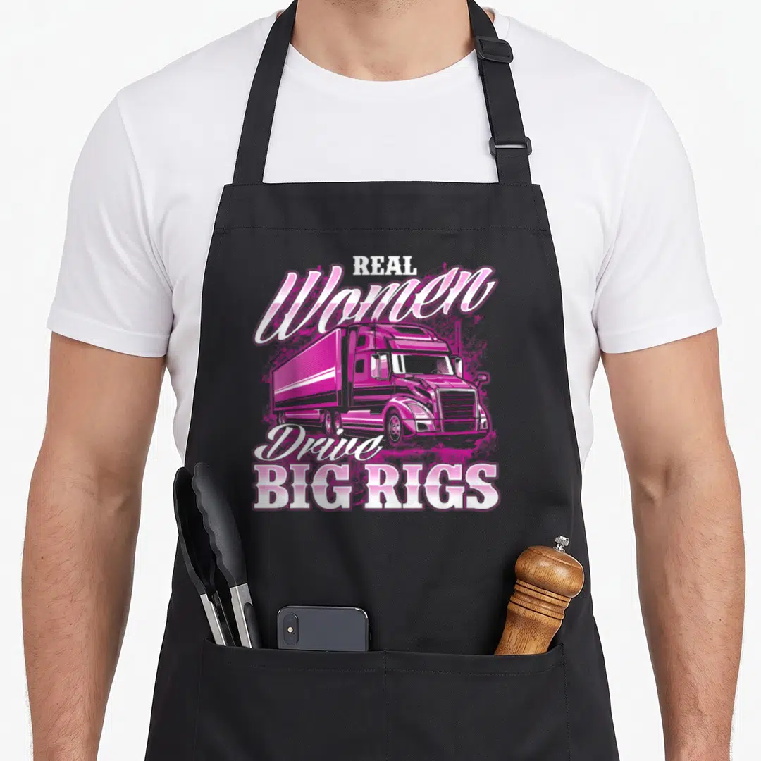 Drive semi truck apron - Pink cartoon semi-truck with Real Women Drive Big Rigs text — shown on a black cotton canvas apron against a white background