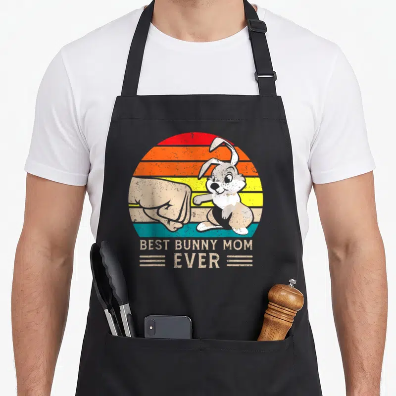 Rabbit hare apron - Retro bunny and fist bumping in front of striped sun with text — shown on a black cotton canvas apron against a white background