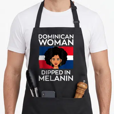 Dipped pride apron - Cartoon woman with afro before Dominican flag text reads Dominican Woman Dipped In Melanin — shown on a black cotton canvas apron against a white background