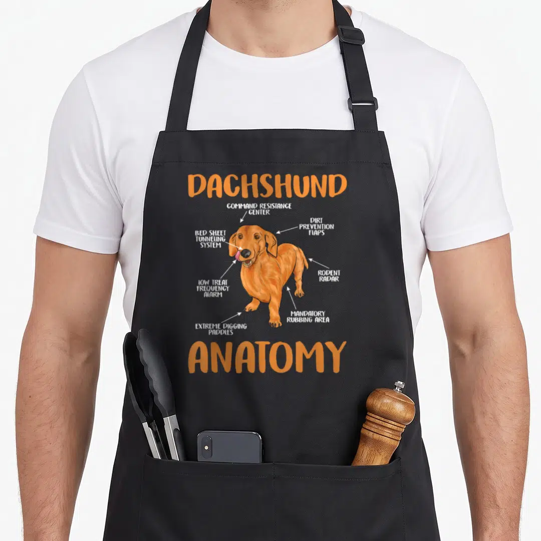 Anatomy wiener apron - Cartoon dachshund labeled with humorous anatomy terms like Rodent Radar and Extreme Digging — shown on a black cotton canvas apron against a white background