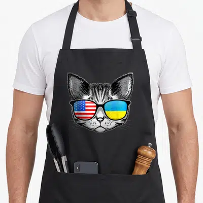 Cat american flag apron - Realistic cat head facing forward wearing sunglasses with US and Ukrainian flag lenses in red — shown on a black cotton canvas apron against a white background