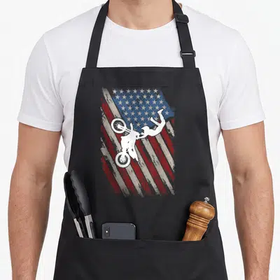 Bike 4th of july apron - White motocross rider silhouette on distressed red white and blue flag — shown on a black cotton canvas apron against a white background