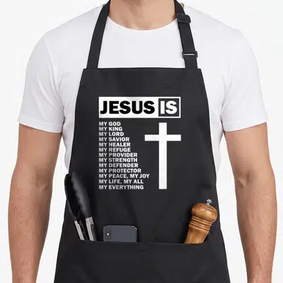 Jesus christ is enough apron - White cross next to stacked list of titles including My God My King My Savior in black — shown on a black cotton canvas apron against a white background