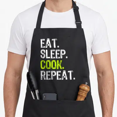 Eat culinary aprons - Stacked EAT SLEEP COOK REPEAT text in white and lime green distressed font — shown on a black cotton canvas apron against a white background