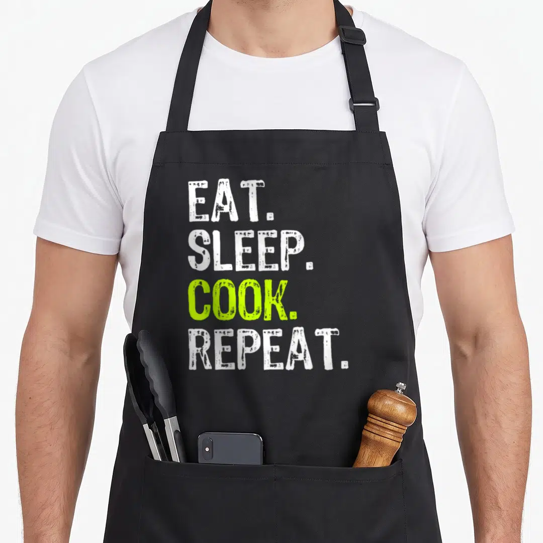 Eat culinary aprons - Stacked EAT SLEEP COOK REPEAT text in white and lime green distressed font — shown on a black cotton canvas apron against a white background