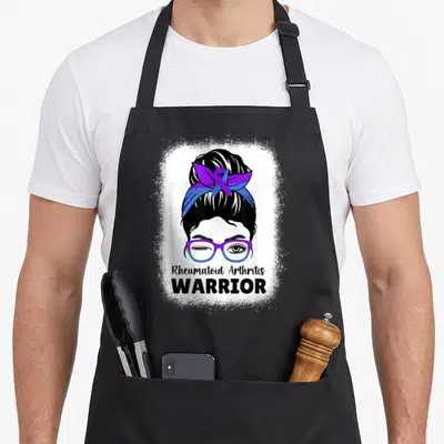 Rheumatoid messy aprons - Woman face winking with purple blue glasses and ribbon headband reading RA Warrior — shown on a black cotton canvas apron against a white background