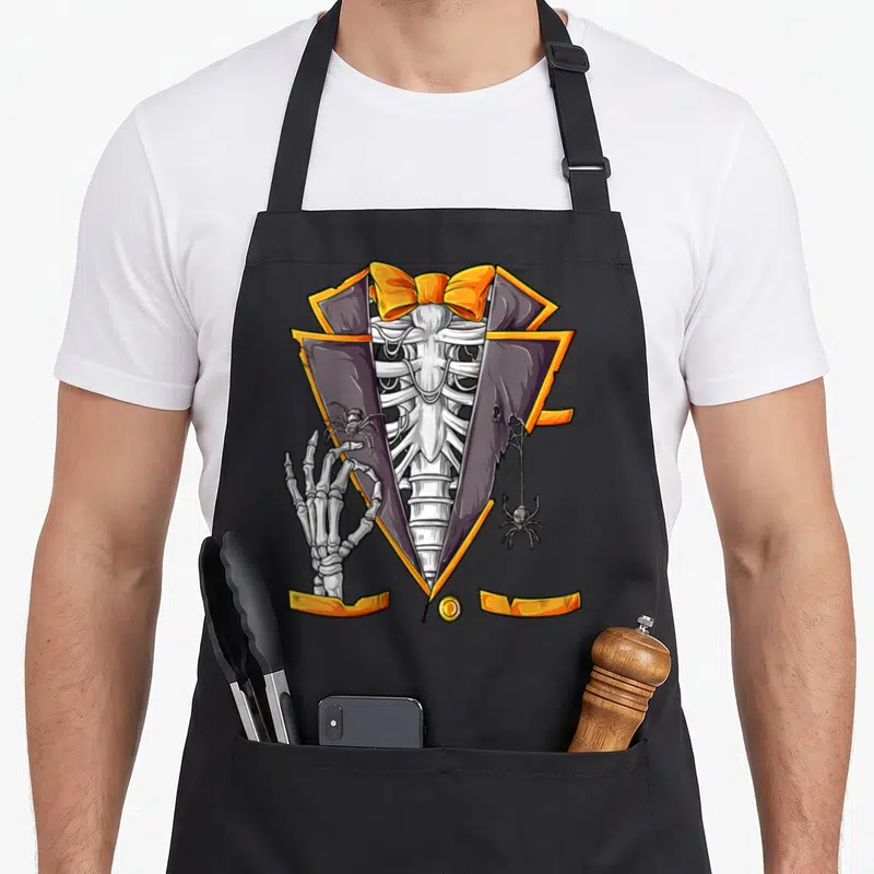 Tuxedo halloween apron - Cartoon skeleton torso in purple orange tuxedo making OK gesture with spider on hand — shown on a black cotton canvas apron against a white background
