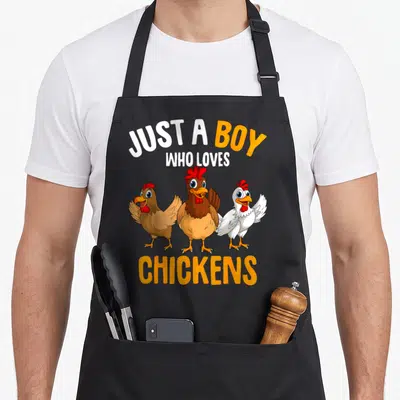 Retro chicken apron - Three cartoon chickens under text reading JUST A BOY WHO LOVES CHICKENS — shown on a black cotton canvas apron against a white background
