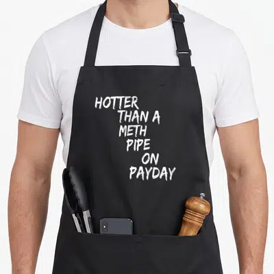 Hotter pipe apron - White stacked text reading HOTTER THAN A METH PIPE ON PAYDAY on black fabric — shown on a black cotton canvas apron against a white background