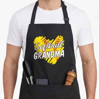 Softball grandma apron - White Softball GRANDMA text over yellow brush stroke and red leaves — shown on a black cotton canvas apron against a white background