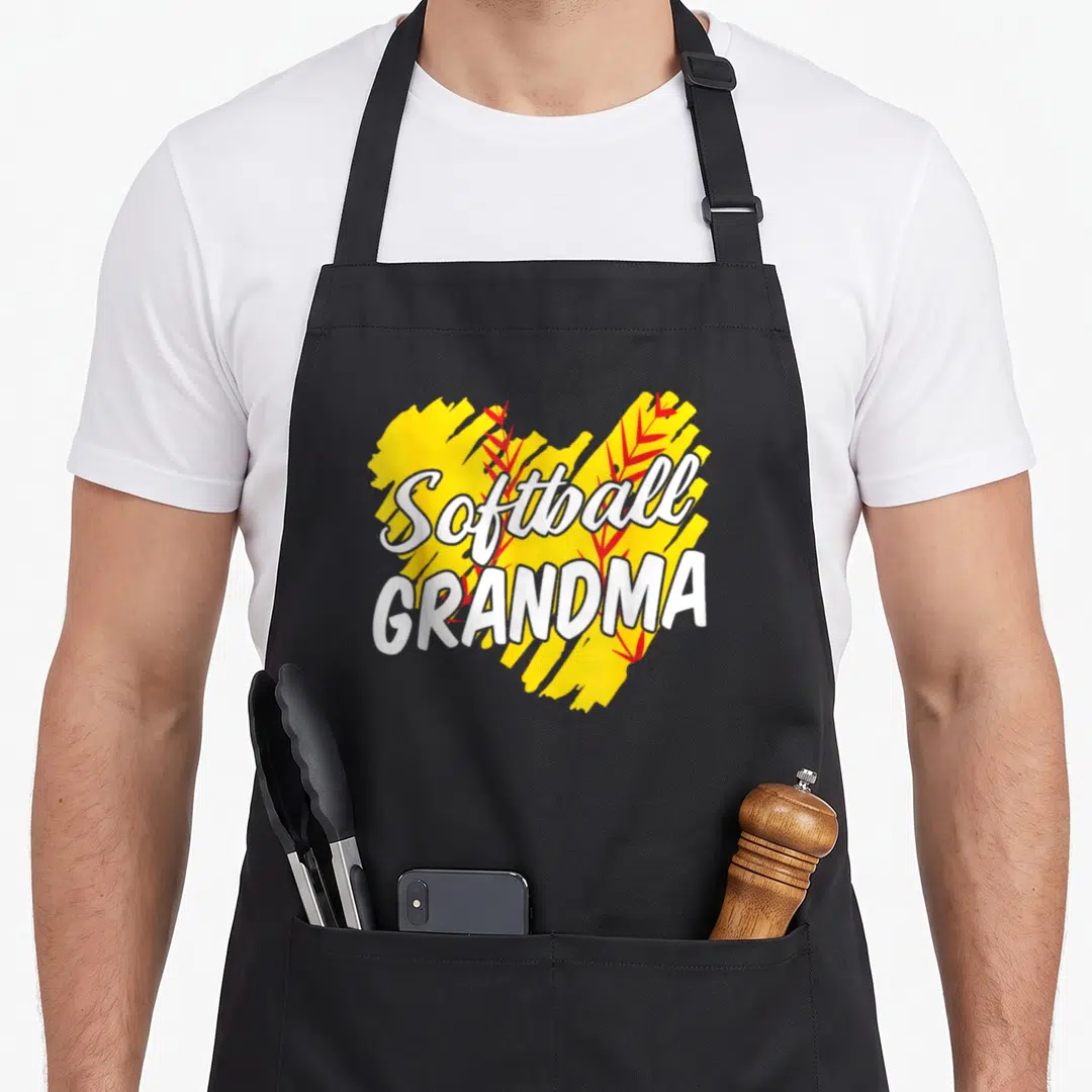 Softball grandma apron - White Softball GRANDMA text over yellow brush stroke and red leaves — shown on a black cotton canvas apron against a white background