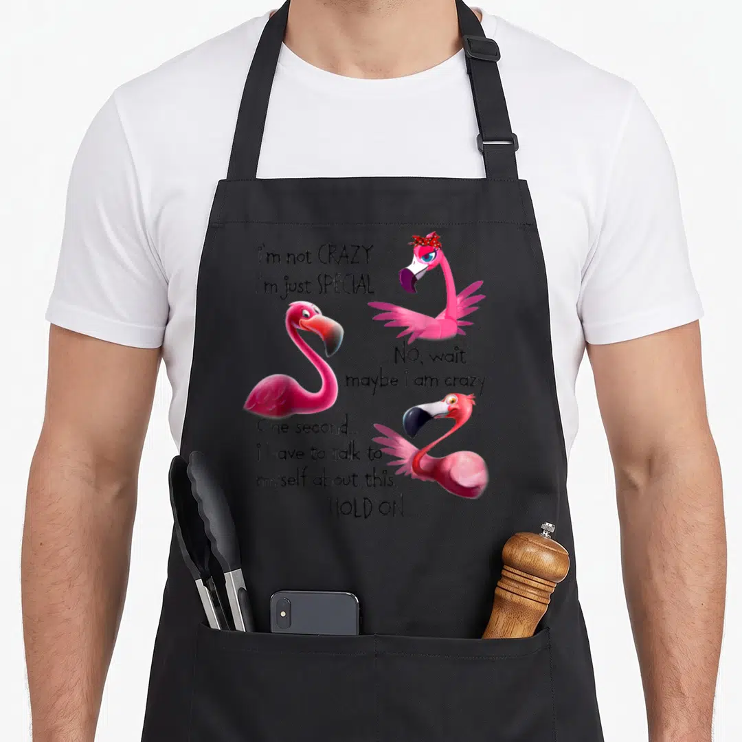 Special flamingo apron - Three pink cartoon flamingos with self-talk quote about being special — shown on a black cotton canvas apron against a white background