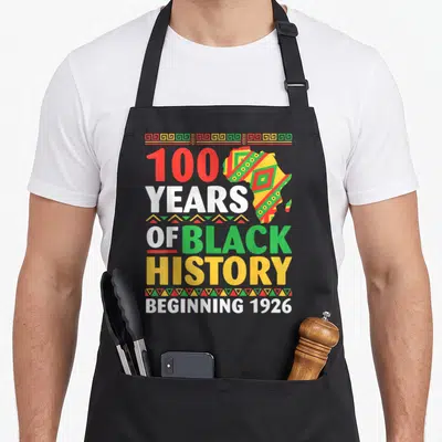 History centennial apron - 100 years of black history beginning 1926 text with patterned africa map and geometric — shown on a black cotton canvas apron against a white background