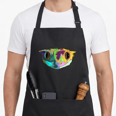 Reptile colourful apron - Cartoon gecko head in yellow, purple, green, blue, and pink — shown on a black cotton canvas apron against a white background