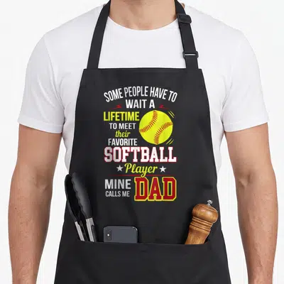Softball playground apron - Stacked text reading Mine Calls Me Dad with yellow softball and two stars — shown on a black cotton canvas apron against a white background