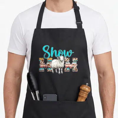 Sheep show mother's apron - Cartoon sheep stands before Show MOM text filled with brown and geometric patterns — shown on a black cotton canvas apron against a white background