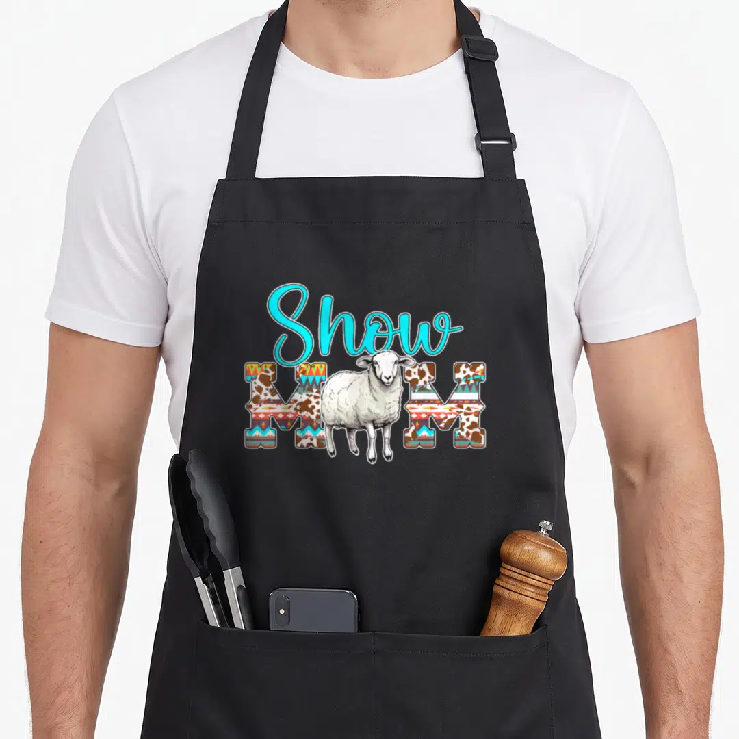 Sheep show mother's apron - Cartoon sheep stands before Show MOM text filled with brown and geometric patterns — shown on a black cotton canvas apron against a white background