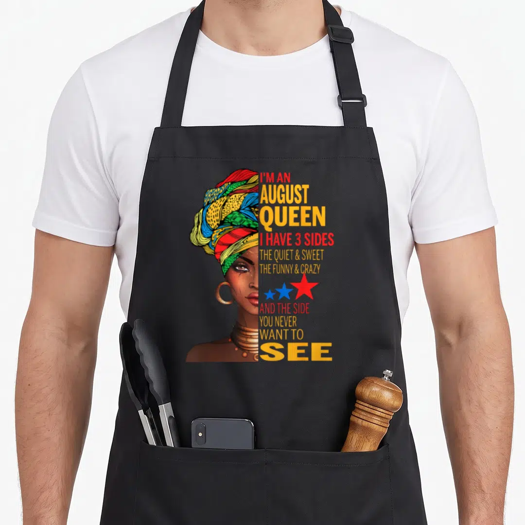 Quite queen apron - Woman headwrap I'M AN AUGUST QUEEN 3 sides text stars yellow red blue green brown — shown on a black cotton canvas apron against a white background