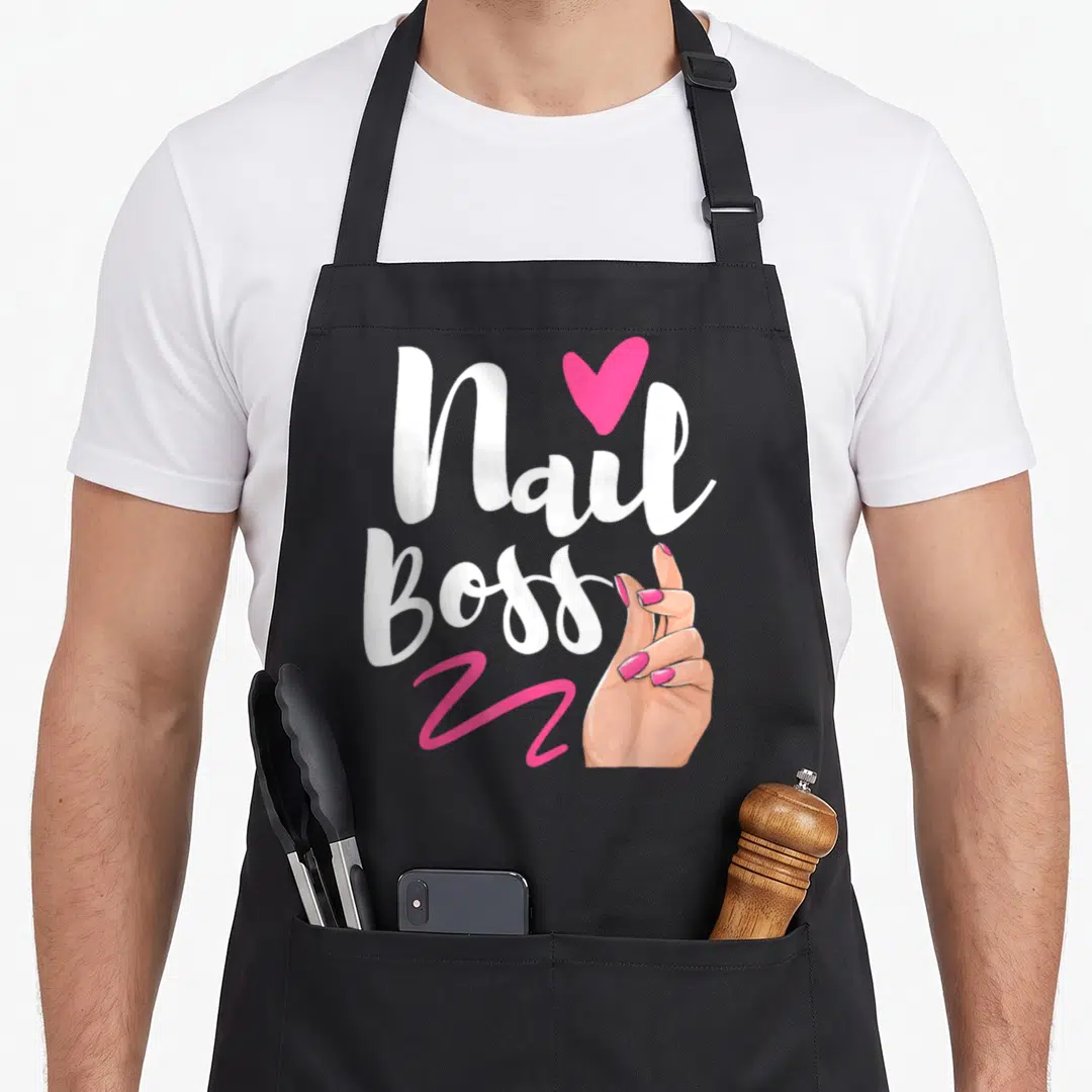 Boss manicurist apron - Nail Boss script with pink heart, squiggle, and hand with pink nails — shown on a black cotton canvas apron against a white background