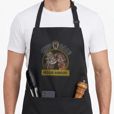 Iconic rangers apron - Chip N Dale Rescue Rangers cartoon logo with acorn and yellow circle border — shown on a black cotton canvas apron against a white background