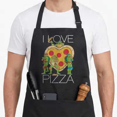 Vintage pizza apron - Four green turtles surrounding a heart-shaped pizza with I LOVE PIZZA text — shown on a black cotton canvas apron against a white background