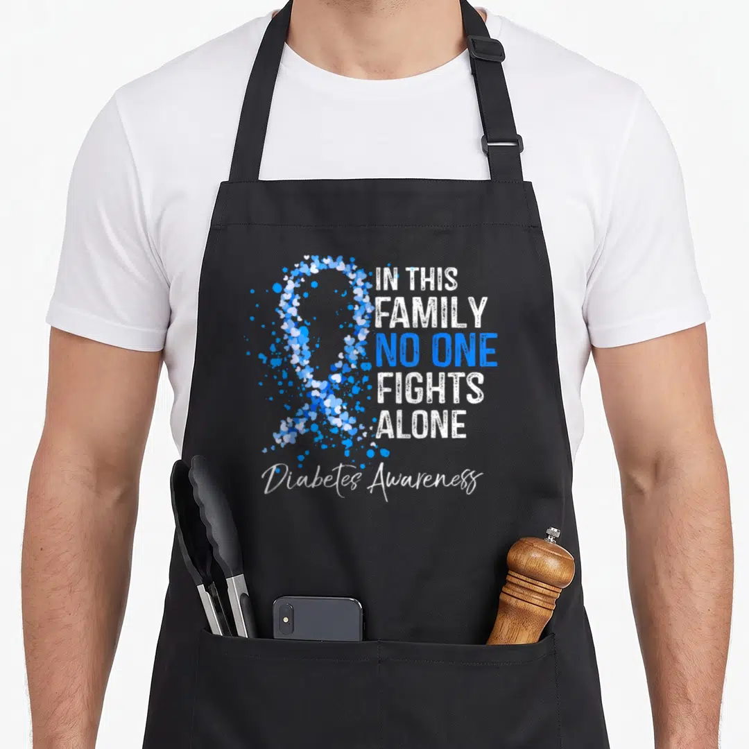 Diabete family aprons - Blue and white ribbon made of hearts with In This Family No One Fights Alone text — shown on a black cotton canvas apron against a white background