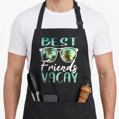Vacay friends cooking apron - BEST Friends VACAY text with white sunglasses showing palm tree reflection in teal — shown on a black cotton canvas apron against a white background