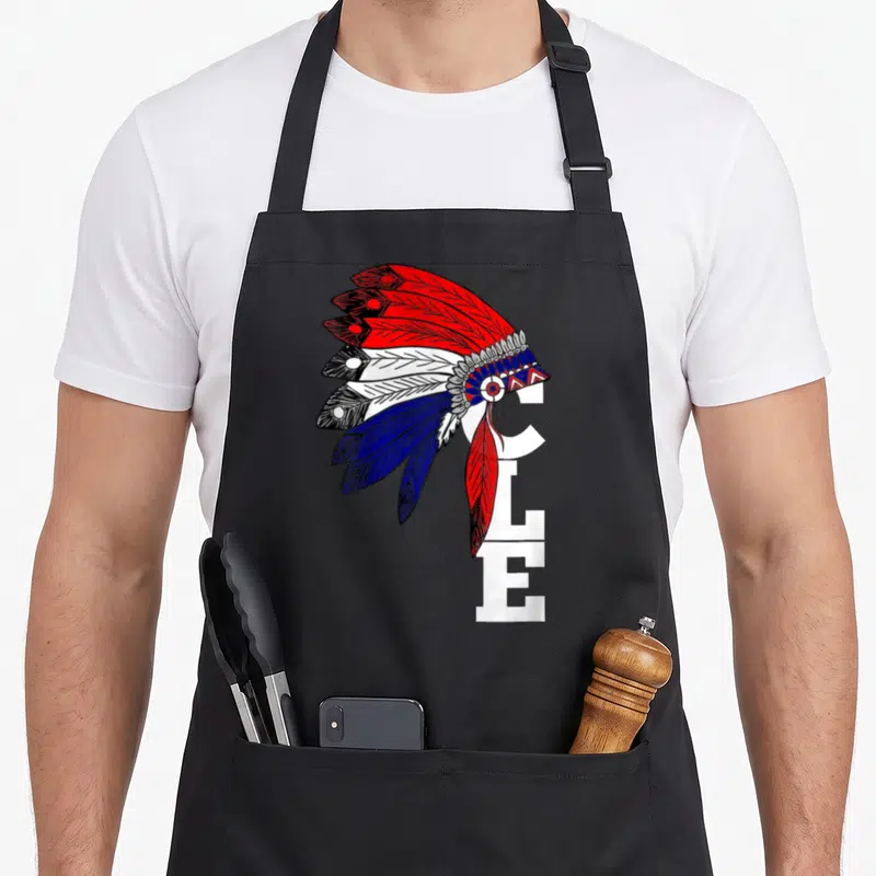 Iroqio cleveland apron - Cartoon headdress in red white blue feathers overlapping vertical white CLE letters — shown on a black cotton canvas apron against a white background