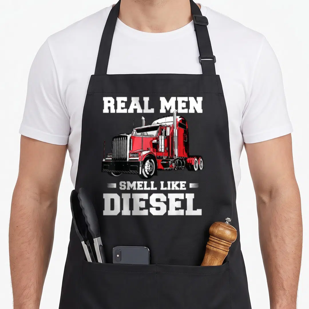 Husband semi truck apron - Red semi-truck illustration with Real Men Smell Like Diesel text — shown on a black cotton canvas apron against a white background