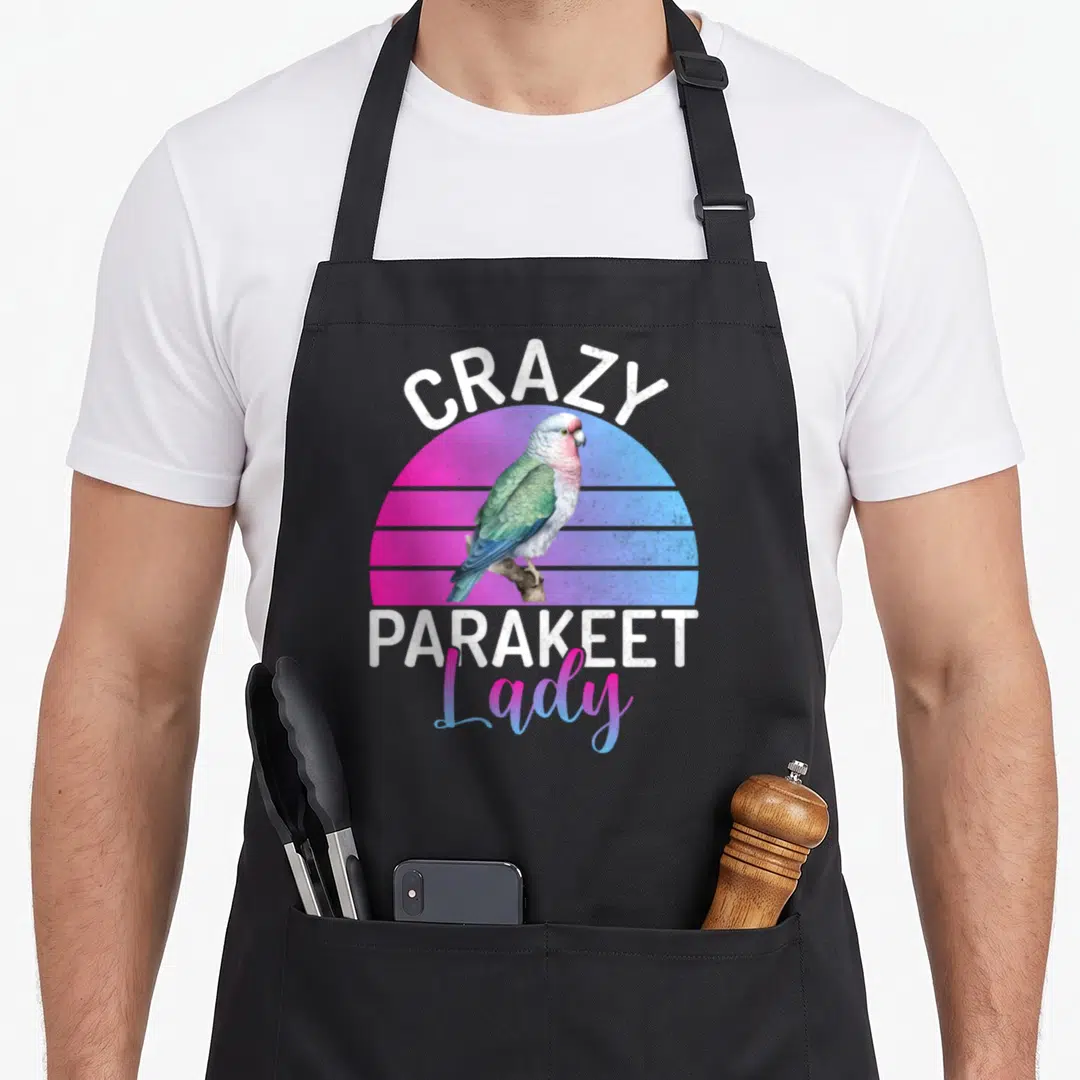 Cute crazy parakeet lady apron - Retro parakeet on pink blue striped sun with Crazy Parakeet Lady text — shown on a black cotton canvas apron against a white background