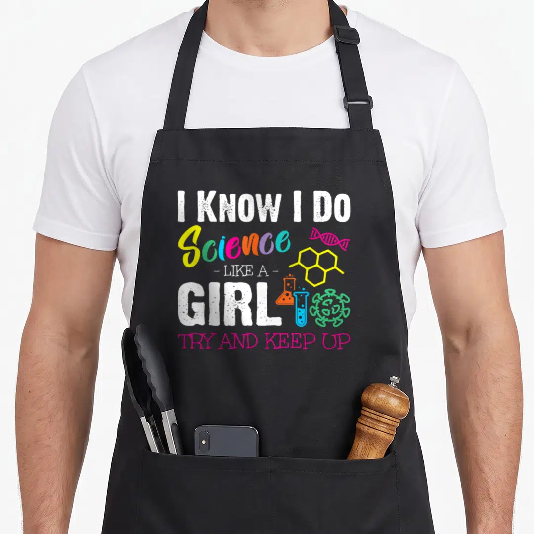 Try science apron - I KNOW I DO Science LIKE A GIRL text with DNA molecule and glassware icons in yellow, green, blue — shown on a black cotton canvas apron against a white background