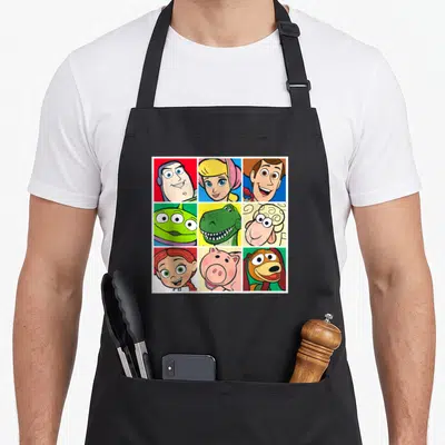 Cast camping apron - Nine cartoon character portraits in a 3x3 grid on red, blue, green, yellow, and pink backgrounds — shown on a black cotton canvas apron against a white background