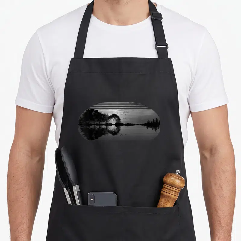 Sky tree apron - Black grey semi-circle landscape with trees city skyline bird reflection water photo style — shown on a black cotton canvas apron against a white background