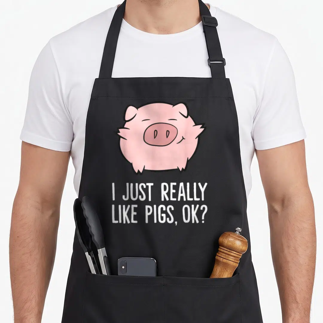 Cute pig lover apron - Round pink cartoon pig above white text I JUST REALLY LIKE PIGS, OK? — shown on a black cotton canvas apron against a white background